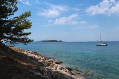 Dalmaçya manzarası, mavi gökyüzü ve berrak turkuaz deniz. Çam ormanları ve yelkenli teknelerle kaplı bir sürü ada.