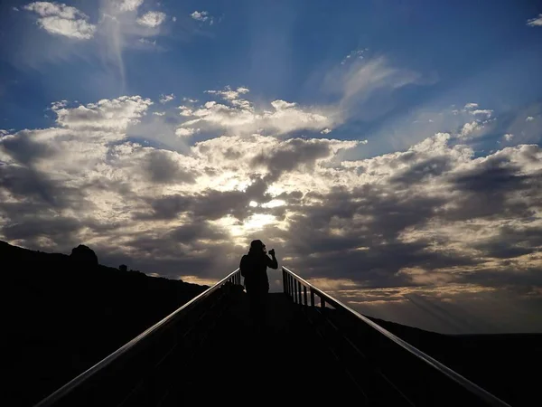 Bir erkek turistin silueti yokuş yukarı yürürken Avustralya çölünde, Tanrı 'nın parlak bir ışığında fotoğraf çekiyor.