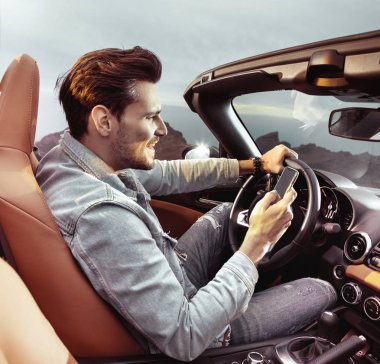Üstü açık bir araba sürme ve cep telefonu tutan yakışıklı adam