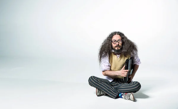 Portrét nerdyho chlapa držícího kufřík a sedícího na bílém — Stock fotografie