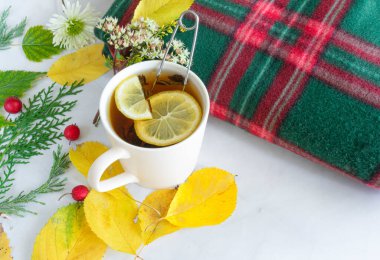 Limonlu çay, çaydanlık, ekose ve sonbahar sarı-yeşil yapraklı çay, beyaz mermer arka planda böğürtlen. Sonbahar kompozisyonu. Sonbahar, Şükran Günü konsepti. Sağlık konsepti, soğuk tedavi. 