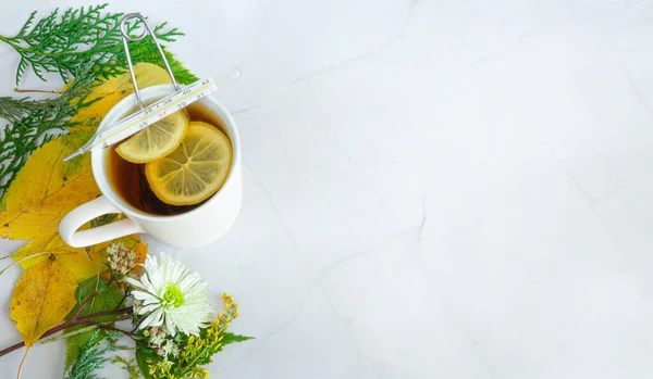 Limonlu çay, termometre ve beyaz mermer arka planda yapraklar. Sıcak sonbahar içkileri. Sonbahar, Şükran Günü konsepti. Sağlık konsepti, soğuk tedavi. Yukarıdan bak. Boşluğu kopyala