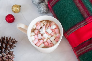 Noel içkileri. Beyaz kahve bardağı, şekerleme ve tarçın, sıcak ekose, kozalak, beyaz mermer arka planda Noel topları. Kış zamanı. Yukarıdan bak. Noel tatili kavramı