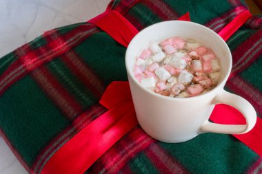 Noel içkileri. Beyaz fincan sıcak çikolata, marşmelov ve tarçınlı, beyaz mermer arka planda sıcak ekose. Kış zamanı. Noel tatili konsepti