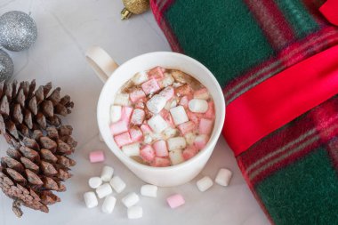 Noel içkileri. Beyaz fincan sıcak çikolata, marşmelov ve tarçın, sıcak ekose, kozalak, beyaz mermer arka planda noel topları. Kış zamanı. Yukarıdan bak. Noel tatili kavramı
