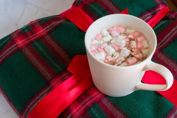 Noel içkileri. Beyaz fincan sıcak çikolata, marşmelov ve tarçınlı, beyaz mermer arka planda sıcak ekose. Kış zamanı. Noel tatili konsepti