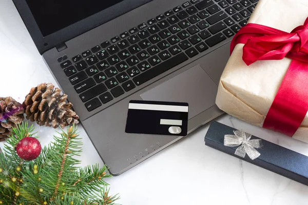 Noel tatili için internetten kredi kartı ve dizüstü bilgisayarla Noel alışverişi. Noel hediyeleri. Kara Cuma. Noel süsleri, hediyeler, defter, beyaz mermer zemin.