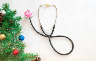 Noel 'i sağlık hizmetlerinde kutluyoruz. Düz bir manzara. Kalp şeklinde oyuncak. Kalp tedavisi konsepti. Beyaz mermer arka planda steteskop. İçinde noel ağacı dalları, kopyalama alanı, pankart olan tıbbi noel kartı.