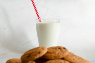 Bardakta süt, yulaf ezmeli kurabiyelerin yanında çikolata parçalı seçici odaklı. Beyaz mermer arka plan. Seçici odaklanma. Yukarıdan bak. Uzayı kopyala Pankart