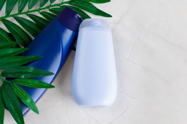 Beyaz mermer arka planda doğal saç bakım ürünleri. Mavi şampuan, maske, merhem, tropik yaprakların üzerindeki duş jeli. Boşluğu kopyala