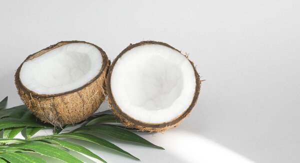 Two halves of coconut and tropical leaves, on a white background. Healthy food. Copy space