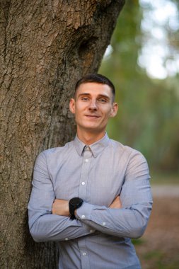 Açık havada bir yaz parkında doğal yeşil arka planda genç bir adamın portresi. Cidden zeki bir adam kameraya bakıp gülümsüyor. Seçici odak