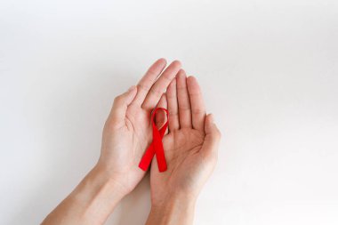 Beyaz arka planda kırmızı kurdele tutan eller, HIV farkındalığı konsepti, Dünya AIDS Günü, Dünya Hipertansiyon Günü, Dünya Kanser Günü.
