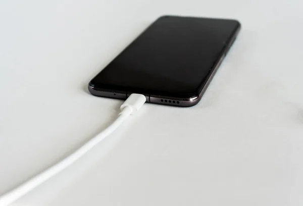 Charging a smartphone via a USB cable on a white background, close up. Silhouette of a black smartphone hanging with a usb charging cable on a white background. Copy space