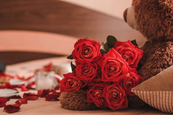 Oyuncak ayı kollarında bir buket gül tutuyor.