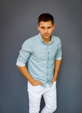 Gri arka planda sıradan giyinmiş, gömlek ve pantolon giymiş genç bir adam.