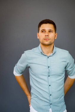 Gri arka planda sıradan giyinmiş, gömlek ve pantolon giymiş genç bir adam.