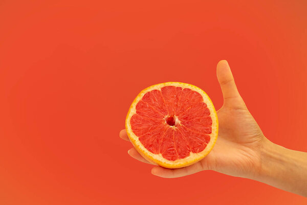 The hand holds half of the grapefruit in the background