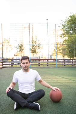 Beyaz tişörtlü genç adam basketbol oynuyor.