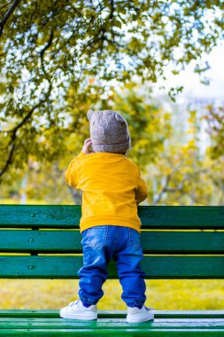 Parktaki bankta duran küçük çocuk. Sarı giyinmiş.