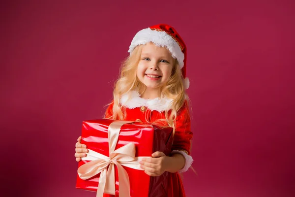 Kleines Blondes Mädchen Weihnachtsmannanzug Mit Einem Neujahrsgeschenk Isoliert Auf Rotem — Stockfoto