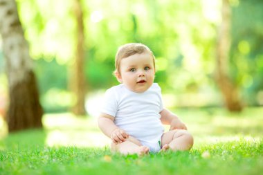 Beyaz elbiseli şirin ve mutlu bir çocuk yeşil yaz çimlerinde oturuyor.