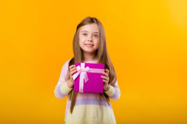 Küçük mutlu bir kızın elinde pembe bir hediye kutusu var. Sarı arka planda izole edilmiş ve mesaj atmak için yeri var.
