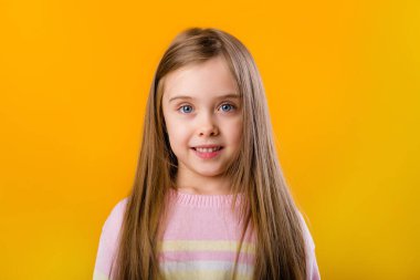 Sarı arka planda izole edilmiş uzun saçlı, gülümseyen küçük bir kızın portresi.