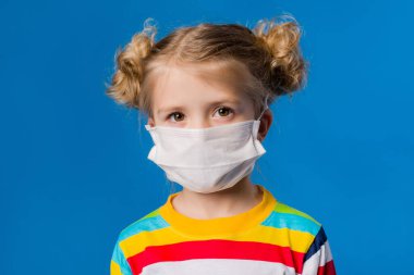 Mavi izole bir geçmişi olan tıbbi maskeli küçük bir kız. COVID-19 'dan koruma kavramı