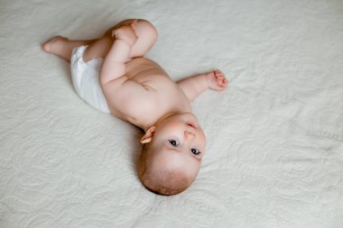 Beyaz yatakta bebek bezi takmış tatlı, mutlu küçük kız. 