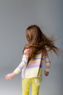 Gri arka planda izole edilmiş uzun saçlı şirin bir kızın portresi.