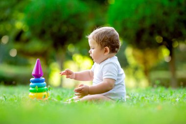 Yazın yeşil çimlerin üzerinde oturan ve çok renkli gelişim piramidi oyuncağıyla oynayan beyaz elbiseli tatlı çocuk.. 