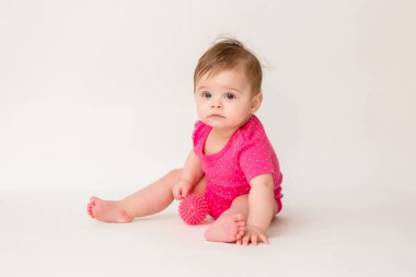 Pembe tişörtlü bir bebeğin yerde oturup lastik topla oynadığı uzay fotoğrafını kopyala