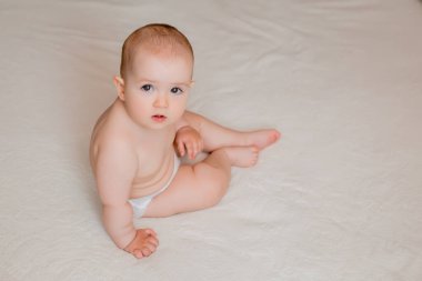 Beyaz yatakta bebek bezi takmış tatlı, mutlu küçük kız. 