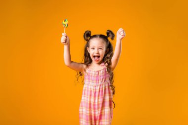 Sarı arka planda lolipopu olan neşeli bir kız. Metnin ya da ilanın için boşluk resmini yerleştirerek kopyala 