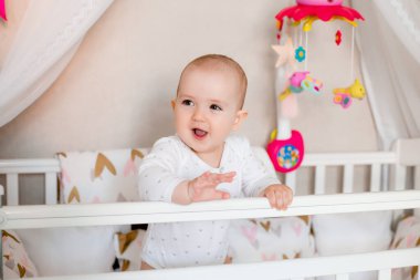 Sevimli küçük kız beşikteki beyaz yatağında renkli oyuncaklar ve yastıklarla