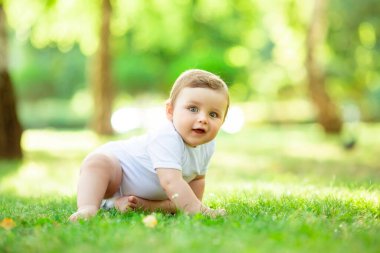 Beyaz elbiseli şirin ve mutlu bir çocuk yeşil yaz çimlerinde oturuyor.