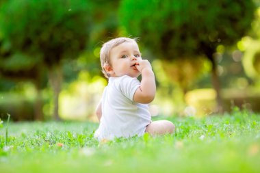 Beyaz elbiseli şirin ve mutlu bir çocuk yeşil yaz çimlerinde oturuyor.