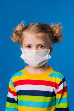 Mavi izole bir geçmişi olan tıbbi maskeli küçük bir kız. COVID-19 'dan koruma kavramı