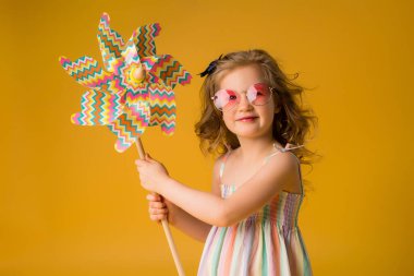 Sarı arka planda fırıldak tutan küçük kız gülümsüyor. Metnin ya da ilanın için boşluk resmini yerleştirerek kopyala