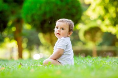 Beyaz elbiseli şirin ve mutlu bir çocuk yeşil yaz çimlerinde oturuyor.