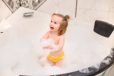 Küçük tatlı kız evde köpükle banyo yapıyor, lastik ördekle oynuyor. 