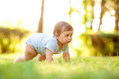 Beyaz elbiseli şirin küçük çocuk emeklemeyi öğreniyor. Sağlıklı çocuk yazın yeşil çimlerde sürünür. 