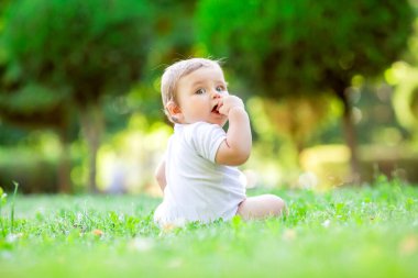 Beyaz elbiseli şirin ve mutlu bir çocuk yeşil yaz çimlerinde oturuyor.