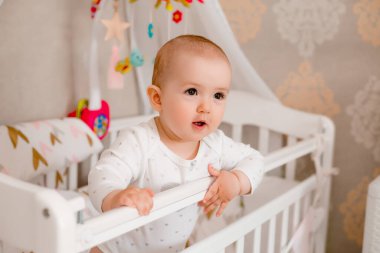 Sevimli küçük kız beşikteki beyaz yatağında renkli oyuncaklar ve yastıklarla