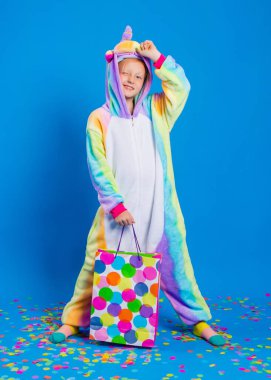 Tek boynuzlu at kostümü giymiş mutlu küçük bir kız elinde renkli konfeti dolu bir hediye çantası tutuyor. Metin için boş alanı olan doğum günü, tatil veya satış kavramı