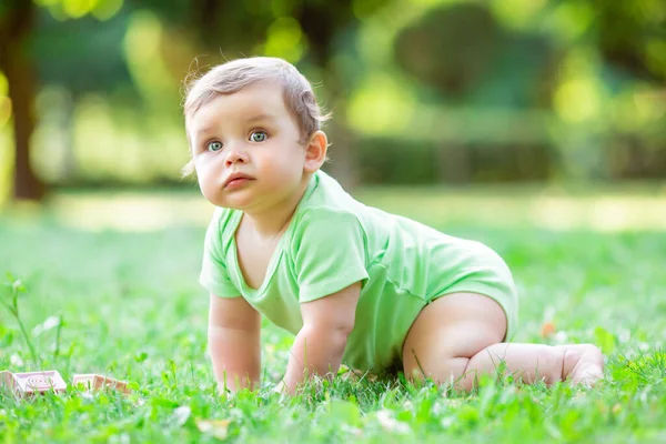 緑のボディスーツのかわいい幼児は夏に草の上を這います 赤ん坊は草の上を這うことを学ぶ — ストック写真