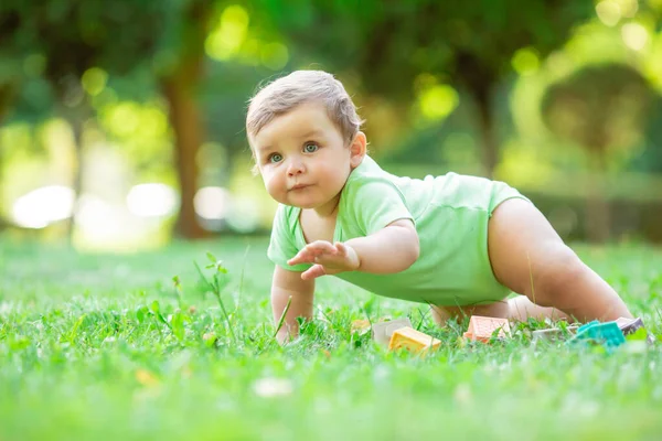 白いボディスーツの可愛い男の子が這うことを学ぶ 健康な幼児は夏に緑の芝生で這う — ストック写真