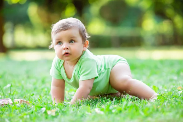 緑のボディスーツのかわいい幼児は夏に草の上を這います 赤ん坊は草の上を這うことを学ぶ — ストック写真