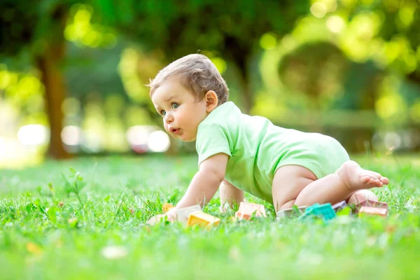 白いボディスーツの可愛い男の子が這うことを学ぶ 健康な幼児は夏に緑の芝生で這う — ストック写真